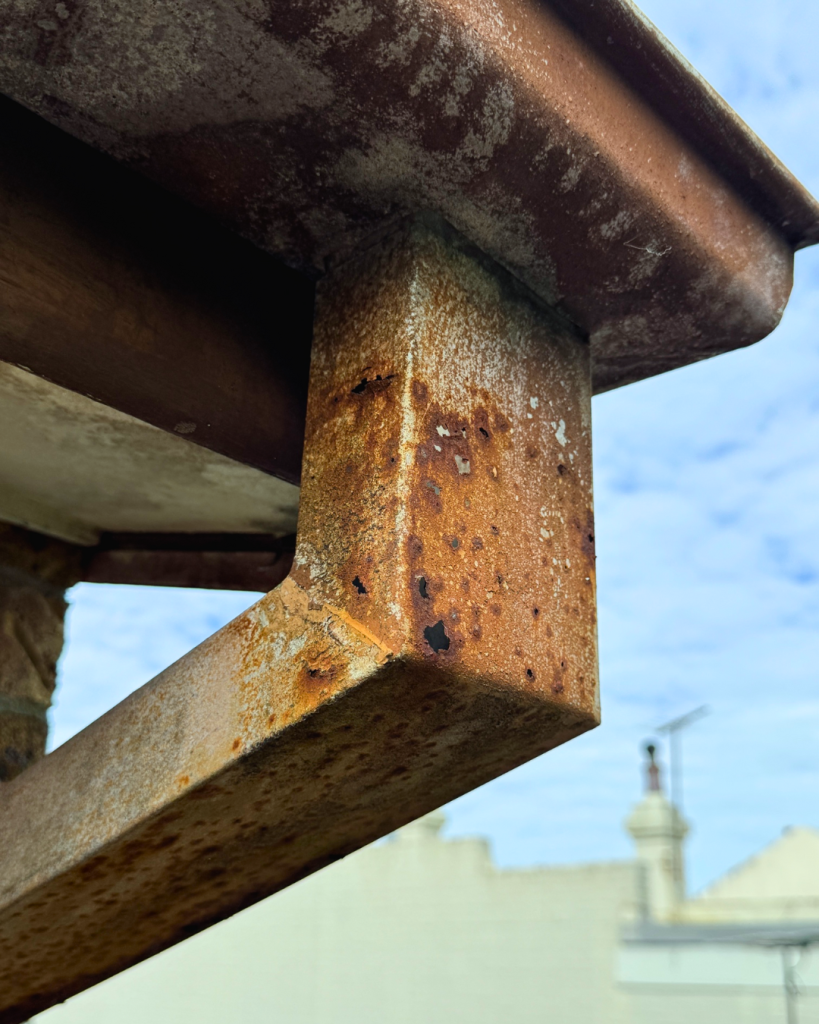 Gutter bracket and fascia heavily corroded with orange surface rust.